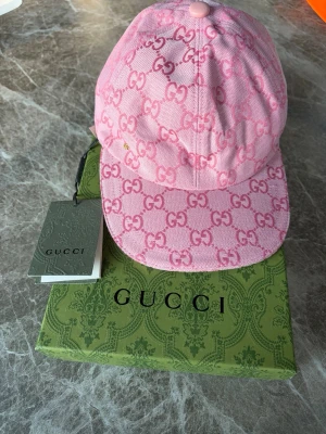 Rosa keps - Säljer en snygg rosa keps från G med det klassiska GG monogrammet över hela kepsen. Kepsen har böjd skärm, justerbart band bak och är tillverkad i canvasmaterial med detaljer i läder. Perfekt för dig som vill sticka ut med en lyxig accessoar.