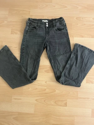 MörkGrå bootcut jeans med dubbla knappar - Snygga grå jeans med bootcut-modell och dubbla knappar i midjan från Gina. Jeansen har bakfickor med lock.💕