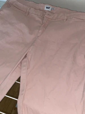 Ljusrosa chinos relaxed fit - Säljer ett par ljusrosa chinos i relaxed fit. Byxorna har klassisk design med bälteshällor och dragkedjegylf. Perfekta för dig som vill ha en avslappnad men ändå stilren look. Materialet känns mjukt och bekvämt.