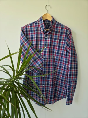 Ralph Lauren - Klassisk rutig skjorta från Ralph Lauren i blått, rött och vitt. Skjortan har lång ärm, knappar framtill och button-down krage. Tillverkad i mjuk bomull och har den ikoniska broderade loggan på bröstet. Stor I storleken.