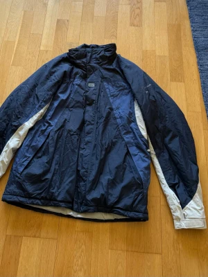 Jacka från Helly Hansen - Säljer en blå jacka med vita detaljer längs ärmarna från Helly Hansen.