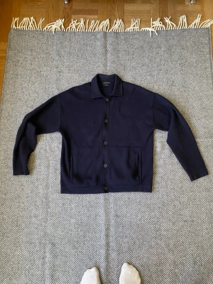 Massimo dutti cardigan / kofta  - Marinblå stickad overshirt/cardigan från Massimo Dutti i storlek M. Tillverkad i ett mjukt och följsamt premiumtyg med stilren krage, knappstängning och två framfickor. Perfekt både som tunn jacka och som lager över t-shirt eller skjorta.  Mycket elegant och tidlös modell som passar lika bra till jeans som kostymbyxor. Ett plagg som fungerar året runt.  Skick: • Mycket fint skick • Inga hål eller fläckar • Endast normalt, minimalt användningsslitage  Storlek: M Färg: Marinblå Märke: Massimo Dutt