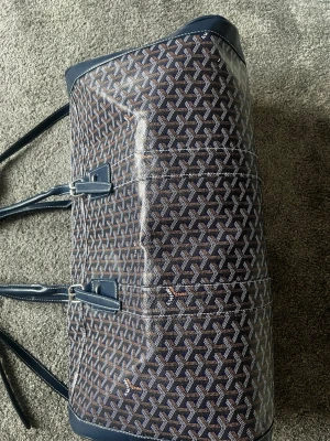 Mönstrad weekendbag  - Snygg weekendbag med klassiskt grafiskt mönster i blått, vitt och brunt. Väskan har detaljer i mörkblått läder, dubbla handtag och silverfärgade metalldelar. Perfekt för resor när du vill ha både stil och funktion.