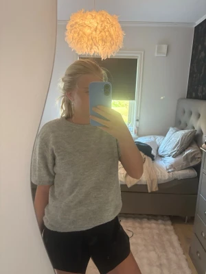Ljusgrå stickad t-shirt - Säljer en ljusgrå stickad t-shirt med korta ärmar och rund halsringning. Tröjan har en enkel och clean design, perfekt att matcha med både jeans och kjol. Materialet ser mjukt och bekvämt ut, och modellen är något boxig för en avslappnad vibe.