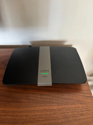 Linksys EA6200 WiFi-router svart - Säljer en svart och grå WiFi-router från Linksys, modell EA6200. Routern har en platt, rektangulär form med ventilationshål på undersidan och tydlig märkning på ovansidan. Perfekt för att förbättra ditt trådlösa nätverk hemma.
