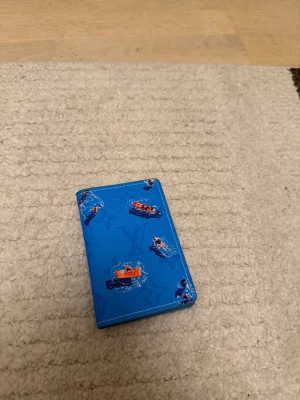Blå plånbok - Säljer en blå plånbok i läder med coola tryck av små båtar och vattenstänk. Plånboken har ett unikt mönster och en ficka på baksidan för kort. Perfekt för dig som vill ha något annorlunda och färgglatt i fickan.