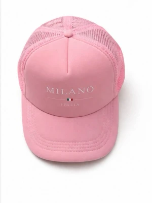 Rosa truckerkeps med Milano-tryck - Snygg rosa truckerkeps med texten 'MILANO ITALIA' och en liten italiensk flagga framtill. Kepsen har böjd skärm och mesh-paneler på sidorna och bak för extra ventilation. Justerbar passform baktill. Perfekt för en trendig och avslappnad stil.