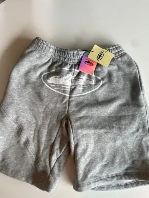 Grå sweatshorts med tryck - Säljer ett par grå sweatshorts med elastisk midja och vitt tryck framtill. Shortsen har fickor på sidorna och en bakficka. Perfekta för chill dagar och har en avslappnad passform.