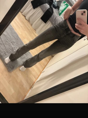 Grå bootcut jeans med hög midja - Snygga grå jeans med bootcut-modell och hög midja. Jeansen har klassiska fem fickor och är tillverkade i ett stretchigt denimtyg som sitter tajt över låren och släpper ut vid vaden. Perfekta för en trendig och avslappnad look.