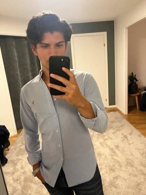 Ljusblå skjorta från Ralph Lauren - Klassisk ljusblå skjorta från Ralph Lauren med button-down krage och broderad logga på bröstet. Skjortan har långa ärmar, vita knappar och är gjord i mjuk bomull. Perfekt till jeans eller chinos för en clean och stilren look. Tveka inte på att skriva om du har frågor eller funderingar🌟😊
