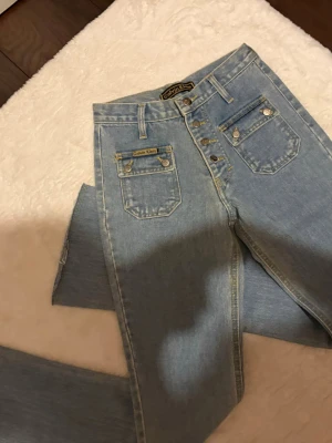 Ljusblå vintage bootcut Calvin Klein - Säljer ett par ljusblå vintagejeans från Calvin Klein med utsvänga  ben och hög midja. Jeansen har klassiska fem fickor, synliga knappar och detaljer i silver. Sparsamt använda och i nyskick, midjemått 32 cm och Innerbenslängd 78 cm