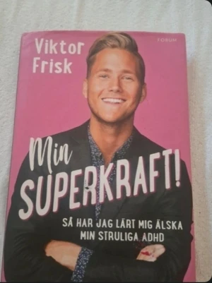 Två inspirerande böcker av Viktor Frisk - Säljer två böcker: 'Min superkraft!' med rosa omslag där Viktor Frisk berättar om sin ADHD, samt 'Samir & Viktor' med svart omslag och porträtt av båda. Perfekt för dig som gillar personliga berättelser och biografier.