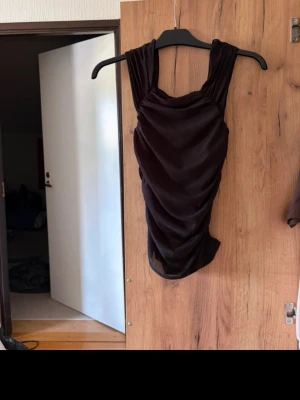 Mörkbrun sammetsklänning - Säljer en svart  kort linne  i mjuk sammet med draperad effekt. Linnet är ärmlös och har breda axelband samt en snygg, kroppsnära passform. Perfekt för dig som vill ha en elegant och trendig look.
