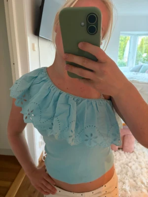 Ljusblå oneshoulder topp med volang - Supersöt ljusblå topp med oneshoulder och bred volang med broderade blommor. Toppen är från Zara och har knappast använt!