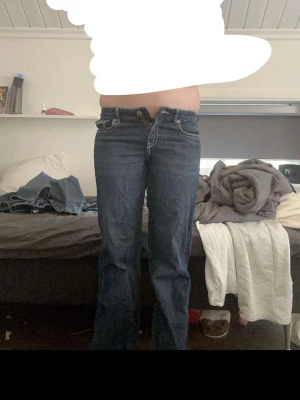 Mörkblå bootcut jeans med kontrastsömmar - Snygga mörkblå bootcut jeans med vita kontrastsömmar och klassiska fem fickor. Jeansen har knapp- och dragkedjestängning samt detaljerade bakfickor med lock. Perfekta för en avslappnad och trendig look.