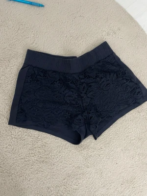 Mörkblå spets-shorts från Terranova - Snygga mörkblå shorts från Terranova med elastisk midja och blommig spetsdetalj framtill. Perfekta för varma dagar och ger en trendig look med sin unika struktur och mjuka material.