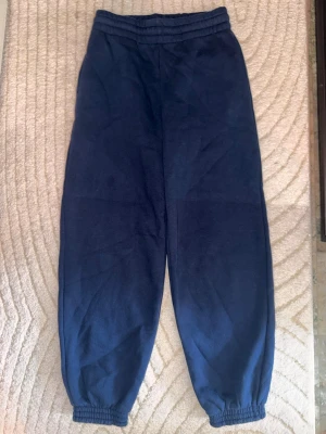 Mörkblå mjukisbyxor med resår - Mörkblå mjukisbyxor med resår i midjan och vid bensluten. Klassisk loose fit-modell i mjukt material, perfekta för chill dagar eller när du vill vara bekväm. Inga synliga loggor eller detaljer, enkel och stilren design.