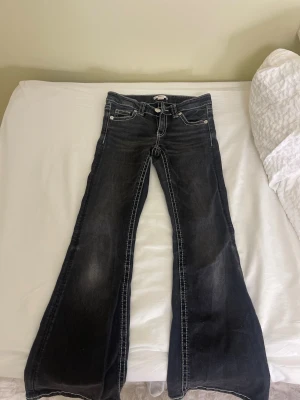 Svarta bootcut jeans med kontrastsömmar - Säljer ett par svarta bootcut jeans med vita kontrastsömmar och snygga broderade bakfickor. Jeansen har klassisk femficksdesign och låg midja. 