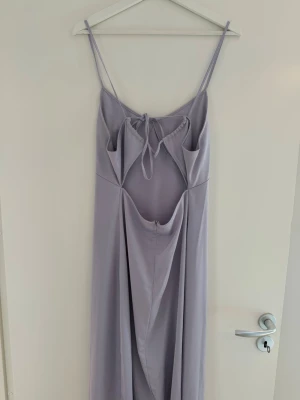 Ljuslila långklänning med knyt - Säljer en elegant ljuslila långklänning med tunna axelband och snygg knytning framtill. Klänningen har en mjuk, följsam passform och ett stilrent, minimalistiskt uttryck. Perfekt för dig som gillar en enkel men chic look.