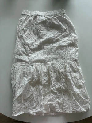 jättegullig vit långkjol från Lindex  - Söt vit långkjol från Lindex med broderade detaljer och lite volang nedtill. Kjolen har resår i midjan. Den är i storlek 134-140cm. Den har som ni kan se på sista bilden ett litet hål men de syns knappt och stör inte på något vis. Säljer för den blivit för liten.