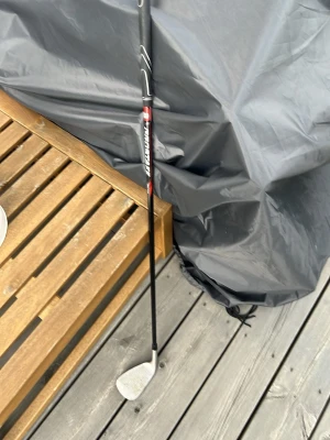 Transmaster golfklubba svart/röd - Golfklubba S (Sandwedge) från Wilson PROSTAFF med svart och rött skaft samt silverfärgat klubbhuvud. Klubbhuvudet har detaljer i svart, rött och vitt och modellen är SDI. Perfekt för dig som vill börja spela golf eller behöver en extra klubba till samlingen. Har använts i 5 rundor efter nyköpt. 