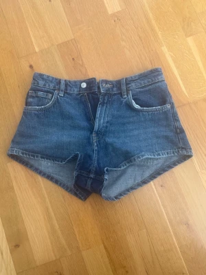 Blå denimshorts - Klassiska blå denimshorts. Shortsen har bälteshällor, knapp och dragkedja framtill samt en avslappnad passform. Perfekta för varma dagar och enkla att matcha med olika toppar.
