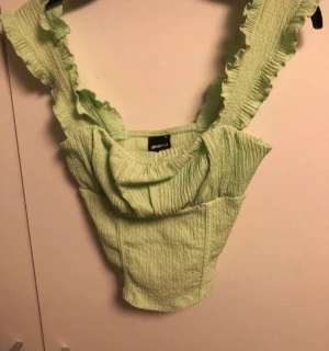 Grön croppad topp med volang - Trendig ljusgrön croppad topp från Gina Tricot med volangkantade axelband och rynkad struktur. Toppen har en fyrkantig urringning och är gjord i ett stretchigt, krinklat tyg som ger en cool och bekväm look.