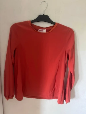 Orange långärmad blus från Dobber - En enkel och stilren orange långärmad blus från Dobber. Blusen har rund halsringning och är gjord i ett mjukt material som känns skönt mot huden. Perfekt att matcha med jeans eller kjol för en clean look nu till hösten 💗