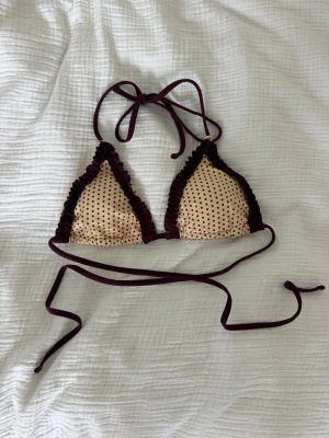 Prickig beige och mörklila bikini - Snygg trekantsbikini med beige bas och små svarta prickar. Bikinin har mörklila volangkant och långa knytband i samma färg. Perfekt för sommaren och strandhäng! Aldrig använd endast testad