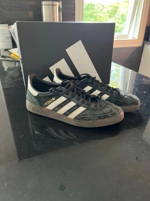 Adidas Spezial svarta sneakers - Svarta Adidas Spezial sneakers med klassiska vita ränder på sidorna och guldfärgad text. Ovandelen är i mocka och sulan är i gummi med tydligt mönster. Låg modell med svart snörning och retrovibe. Perfekta för dig som gillar streetwear och sportig stil.som man ser på bild 4 5 har de släppt en del där av priset  
