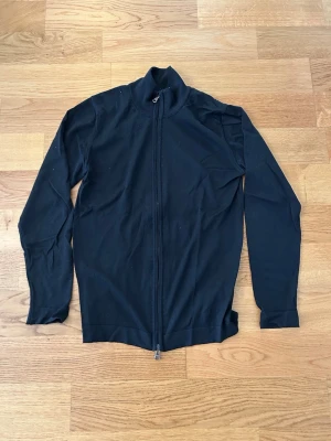 Svart ziptröja från Oscar Jacobson - Klassisk svart ziptröja från Oscar Jacobson med hög krage och hel dragkedja framtill. Tillverkad i mjukt material och har långa ärmar. Perfekt för en stilren och enkel look.