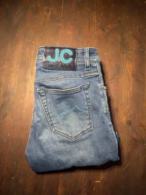 Jacob cohen - Snygga blå jeans från JC med klassisk femficksmodell och ljusare tvätt. Jeansen har kontrastsömmar i turkost och en stor JC-logga på bakfickan. Perfekta för en avslappnad och trendig look.