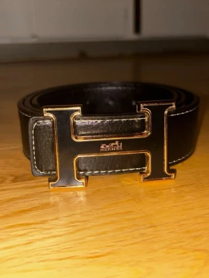 Svart skärp med H-spänne - Snyggt svart skärp med det ikoniska H-spännet i metall. Skärpet är gjort i slätt skinn och har stilrena sömmar längs kanterna. Perfekt accessoar för att lyfta vilken outfit som helst.