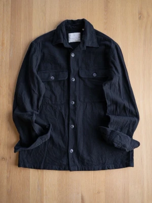 Svart overshirt från Jack & Jones - Stilren svart overshirt från Jack & Jones med klassisk krage, knäppning framtill och två bröstfickor med lock och knapp. Tillverkad i ett mjukt tyg som ger en avslappnad look. Perfekt att bära över en t-shirt för en casual vibe.