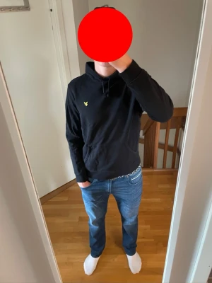 Lyle and Scott hoodie - Säljer en svart hoodie med huva och dragsnören. På bröstet finns en liten gul logga. Hoodien har en klassisk känguruficka framtill och ribbade muddar vid ärmslut och nederkant. Perfekt för en chill och avslappnad stil.