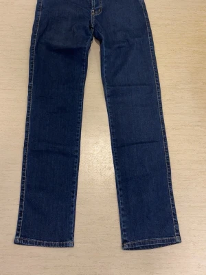 Mörkblå raka jeans från ASUS - Snygga mörkblå jeans från ASUS med raka ben och klassisk femficksmodell. Jeansen har synliga kontrastsömmar och knäppning med tre metallknappar framtill. Perfekta för en avslappnad och stilren look.