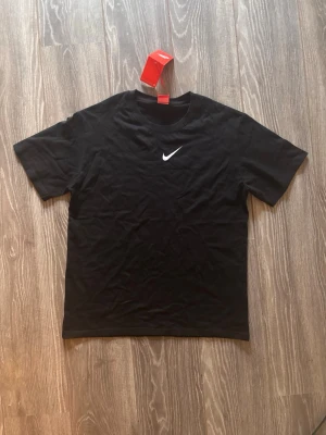 Svart Nike NOCTA t-shirt - Snygg svart t-shirt från Nike NOCTA med vit Nike-logga på bröstet och stor NOCTA-text på ryggen. Klassisk passform och korta ärmar, perfekt till streetwear-looken. Tillverkad i mjuk bomull för skön känsla hela dagen.