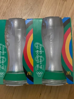 Coca-Cola glas London 2012 OS - Säljer två samlarglas från Coca-Cola, utgivna till London 2012 Olympic Games. Glasen är genomskinliga med gröna detaljer och har OS-logga samt McDonald's-märke på förpackningen. Perfekt för dig som gillar unika samlarprylar eller OS-minnen.