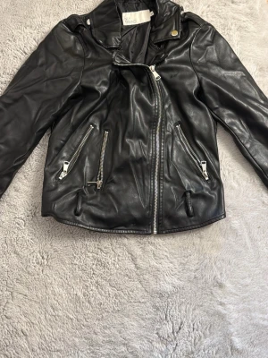 Svart skinnjacka från NLY Trend - Snygg svart skinnjacka från NLY Trend med silvriga dragkedjor och cool bikerkrage. Jackan har två snedställda fickor med dragkedja och en asymmetrisk dragkedja framtill. Perfekt för dig som vill ha en edgy look.
