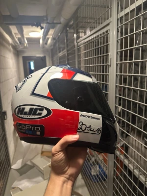 HJC racinghjälm med dekaler - Säljer en snygg racinghjälm från HJC med coola dekaler från GoPro, Deus och Druid Performance. Hjälmen är vit, röd och svart med visir och sportig design. Perfekt för dig som gillar motorsport och vill sticka ut på banan.