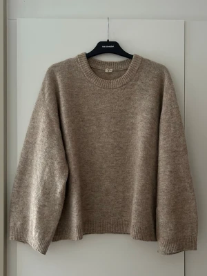 Beige stickad tröja från Arket - Mysig beige stickad tröja med avslappnad, oversized passform och rund halsringning. Tröjan har ribbade muddar vid ärmslut och nederkant. Perfekt för lager på lager och enkel att styla till olika outfits🌤️
