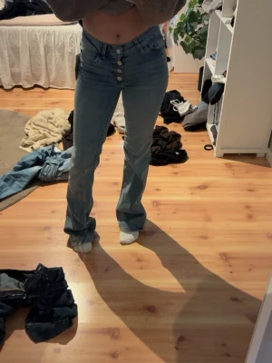 Ljusblå bootcut jeans med knappar - Säljer ett par ljusblå bootcut jeans med mid waist midja och fyra synliga knappar framtill. Jeansen har en klassisk femficksmodell och är tillverkade i ett mjukt denimtyg. Perfekta för dig som gillar en avslappnad men ändå trendig look. Dem är helt nya, aldrig använda och prislapppen är på🫰🏼💕