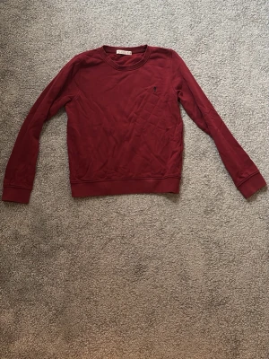 Mörkröd sweatshirt med rund hals - En mörkröd sweatshirt med rund halsringning och långa ärmar. Tröjan har ribbade muddar vid ärmslut och nederkant samt en liten diskret logga på bröstet. Passform: slim fit