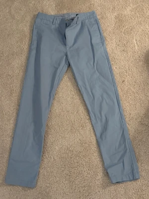 Ljusblå chinos från Polo Ralph Lauren - Snygga ljusblå chinos från Polo Ralph Lauren med klassisk rak passform och dragkedjegylf. Byxorna har bälteshällor och är tillverkade i ett mjukt bomullstyg som känns bekvämt hela dagen.