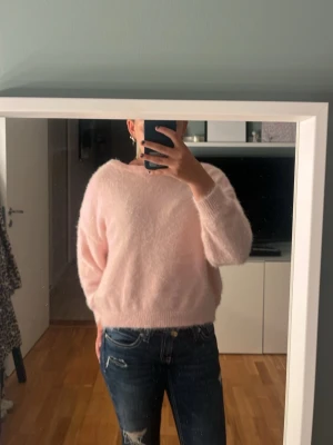 Ljusrosa fluffig stickad tröja - Mysig ljusrosa stickad tröja med fluffig yta och avslappnad passform. Tröjan har rund halsringning, långa ärmar och ribbade muddar vid ärmslut och nederkant. Perfekt för kalla dagar och enkel att matcha med jeans eller kjol.💗