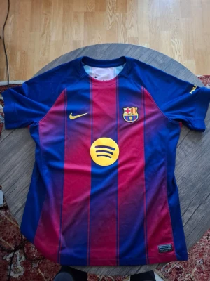 FC Barcelona matchtröja blå/röd - Säljer en officiell FC Barcelona matchtröja från Nike i klassiska blå och röda vertikala ränder. Tröjan har klubbmärke, Nike-logga och Spotify som sponsor framtill samt UNHCR-logga bak. Tillverkad i lätt och ventilerande material, perfekt för fotboll eller träning.
