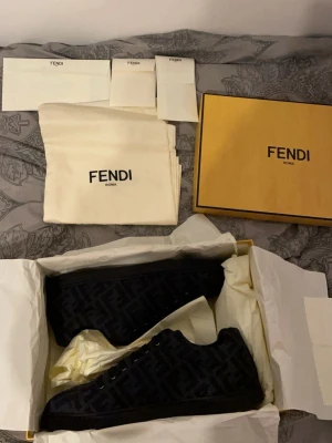 Svarta Fendi sneakers med monogram - Snygga svarta sneakers från Fendi med diskret monogrammönster över hela skon. Lågt skaft och klassisk siluett. Skorna har svarta snören och sula, och är tillverkade i en mix av mocka och textil. Perfekta för dig som gillar exklusiv streetwear. Vid snabbaffär kan priset diskuteras! (Äkta kvitto finns)