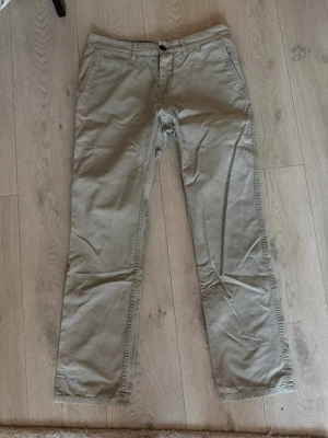 Beige chinos med raka ben - Snygga beige chinos med klassisk passform och raka ben. Byxorna har två sidofickor fram och två bakfickor med knapp. Tillverkade i ett mjukt bomullsmaterial som ger en avslappnad men stilren look. Perfekta för dig som gillar enkel och clean stil.