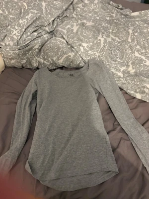 Grå långärmad topp i bomull - En enkel och stilren grå långärmad topp med rund halsringning. Tillverkad i mjukt bomullsmaterial som känns skönt mot huden. Perfekt basplagg att matcha med olika outfits och funkar året runt.