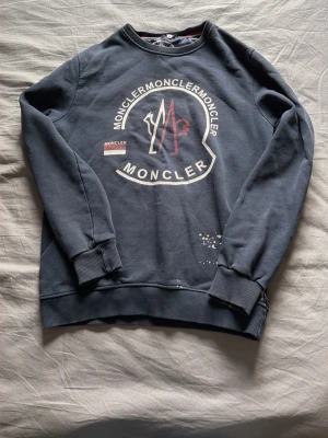 Mörkblå sweatshirt från Moncler - Snygg mörkblå sweatshirt från Moncler med stort tryck och logga på bröstet samt en liten patch på ärmen. Tröjan har rund halsringning, ribbade muddar och är tillverkad i mjukt bomullsmaterial. Perfekt för en avslappnad och trendig look. Storlek m/s